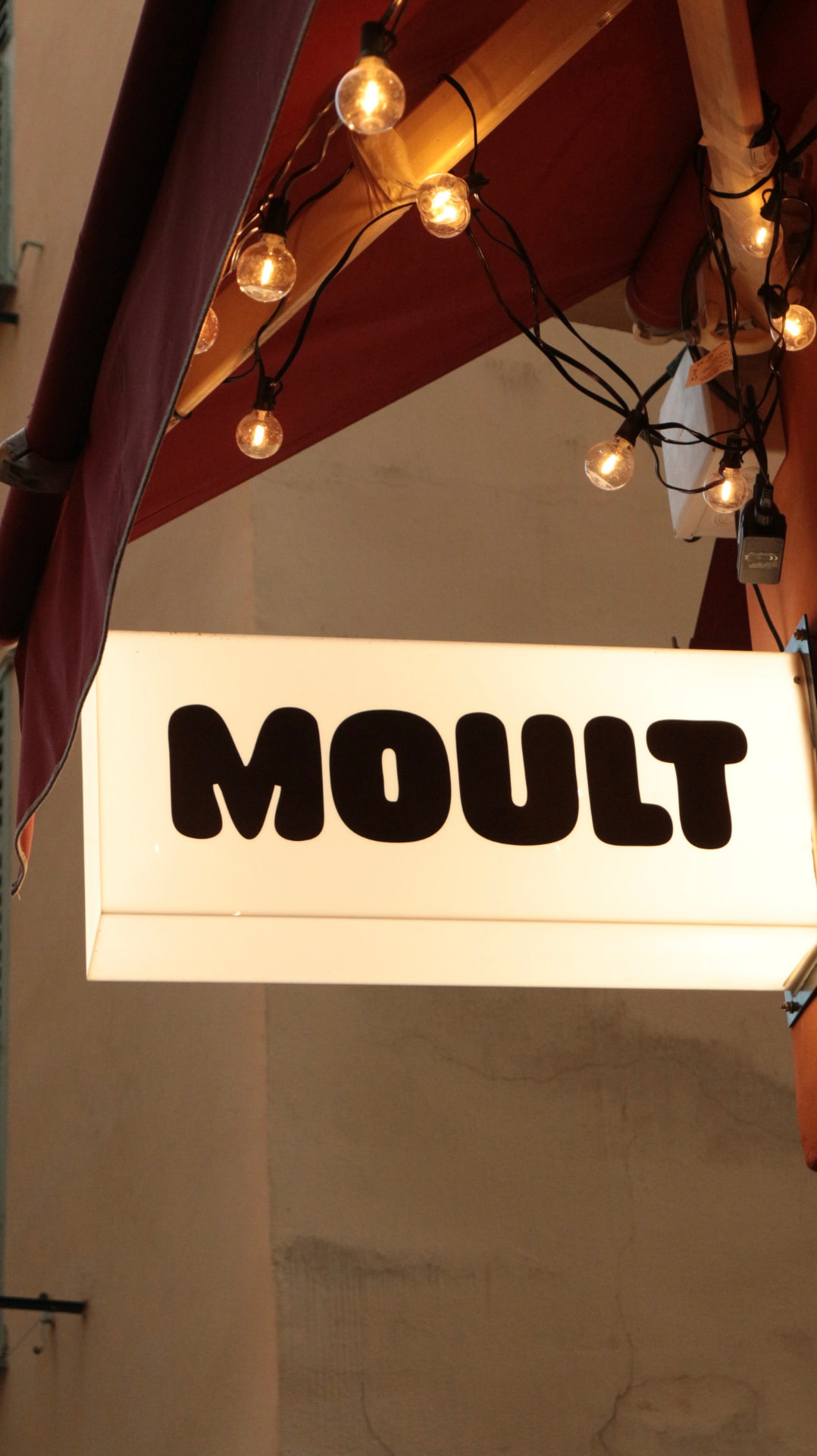 Enseigne lumineuse de Moult sous une guirlande de terrasse